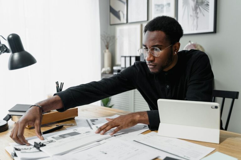 Business professional working at desk reviewing financial documents with digital tablet.